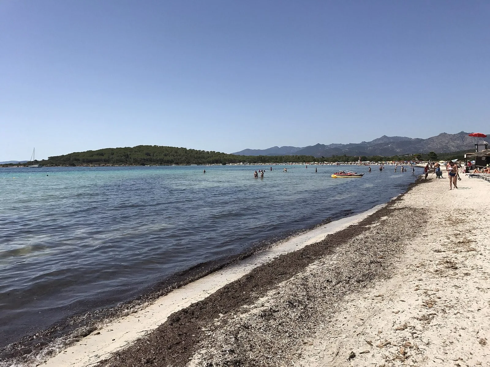 Spiaggia di sabbia chiara a Cala Brandinchi, San Teodoro, con mare limpido e montagne sullo sfondo