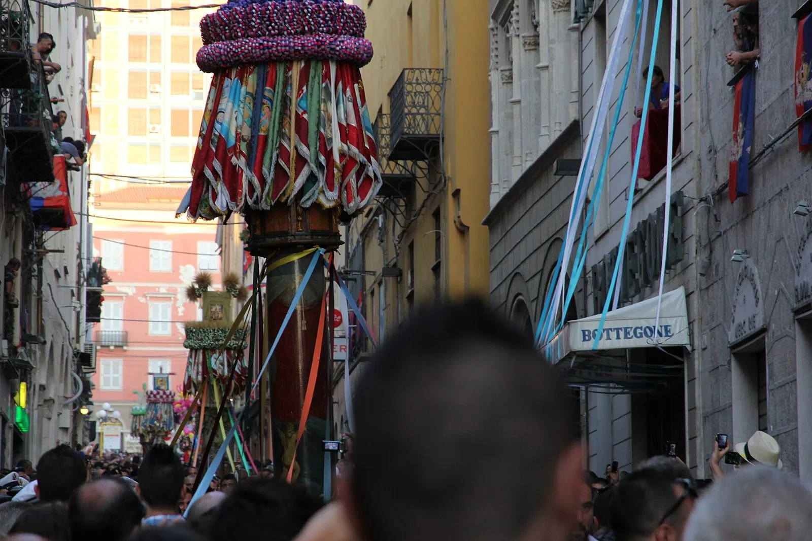 Un candeliere addobbato con drappi e nastri colorati avanza tra la folla in una via del centro storico di Sassari