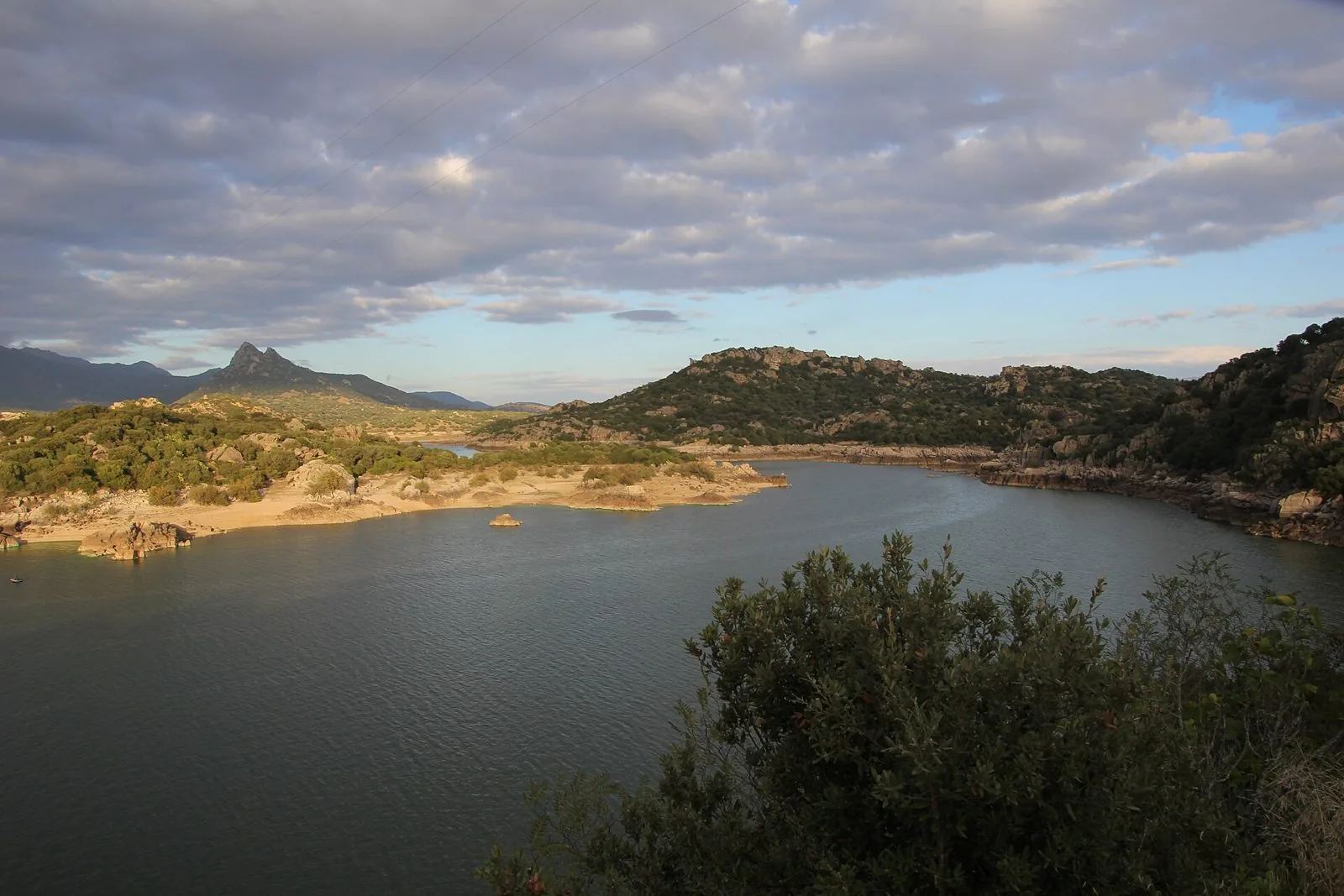 Il lago Coghinas tra colline di granito e macchia mediterranea sotto un cielo nuvoloso nel territorio di Oschiri