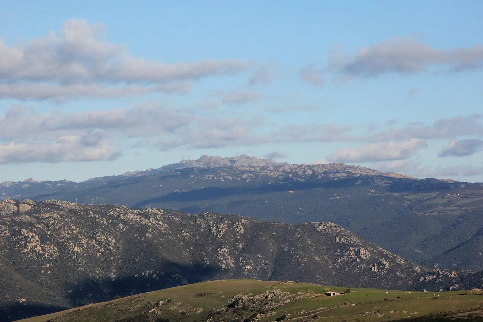 Il massiccio granitico del Monte Limbara sotto un cielo azzurro con nuvole, colline verdi in primo piano